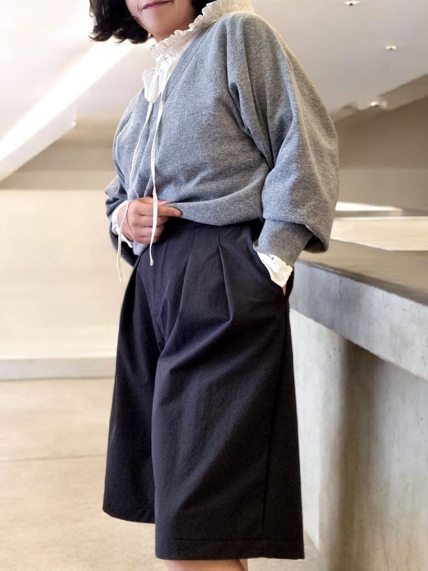 Model wearing charcoal wide-leg pants leaning on counter – side view