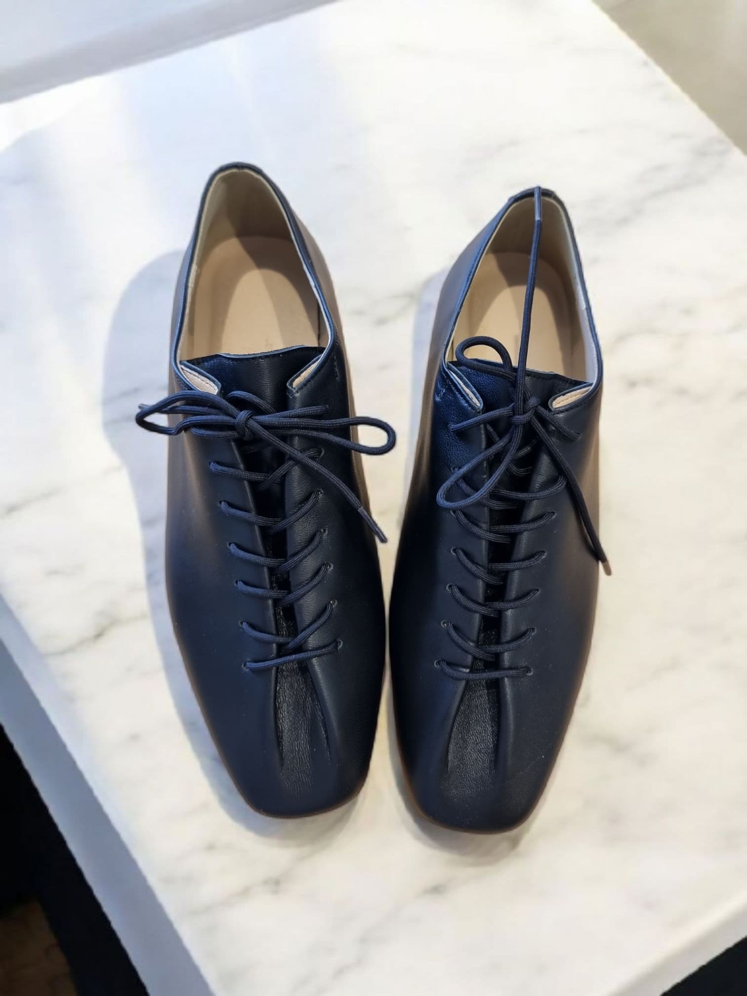 Pair of black leather lace-up shoes on marble – top view