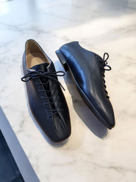 Black leather lace-up shoes placed on a marble surface – angled view
