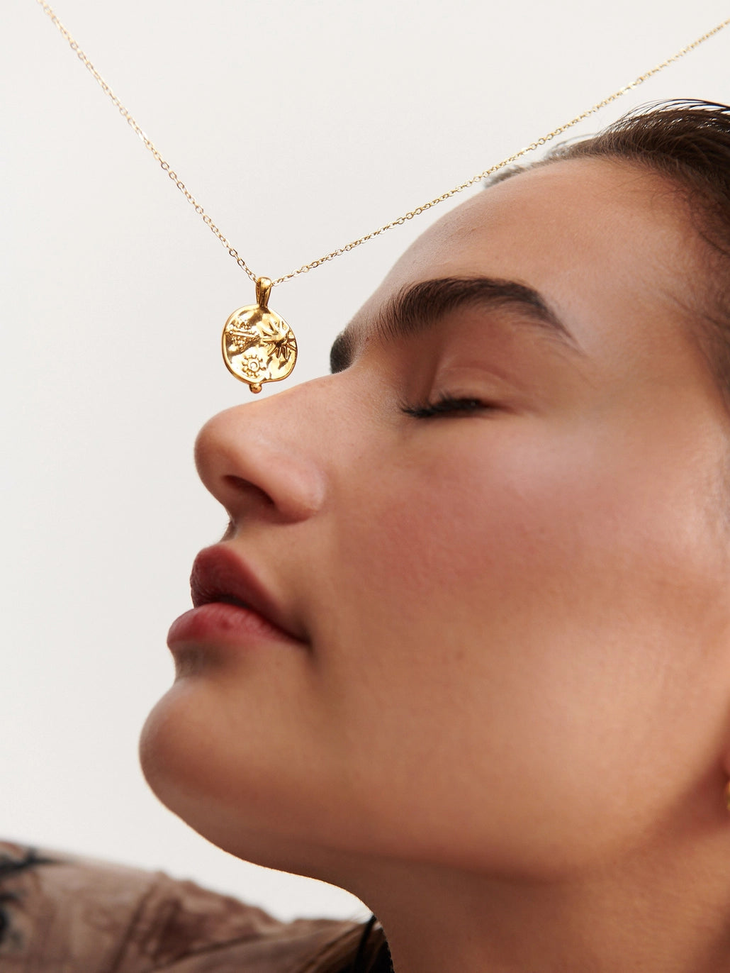 Close-up of a gold medallion necklace with engraved botanical and sun motifs, photographed in warm natural light.
