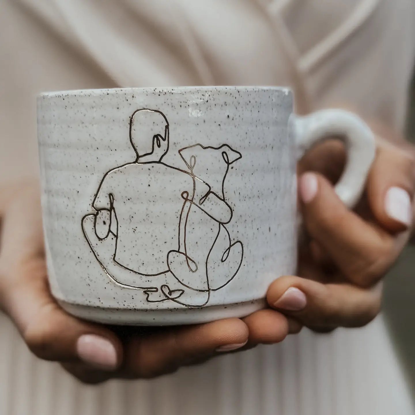 “Person holding a handmade ceramic mug with a line-art design of a man and a dog.”