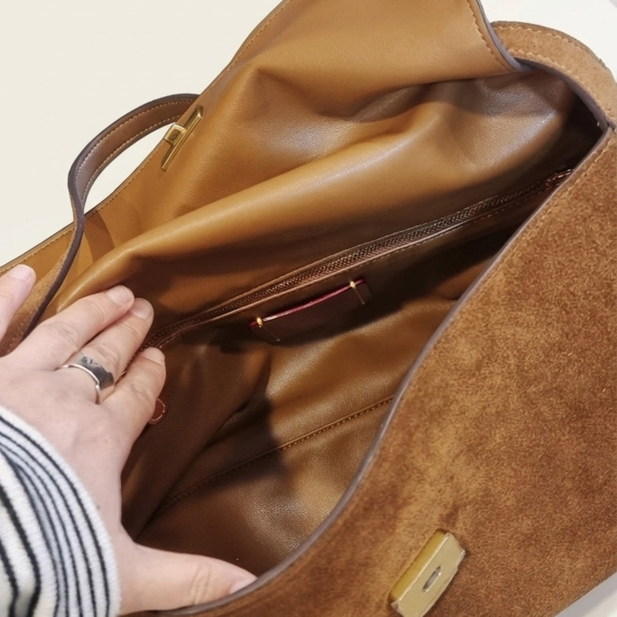 Close-up of a brown suede and leather handbag interior, showing a hand reaching in to demonstrate the spacious zippered pocket and lining.
