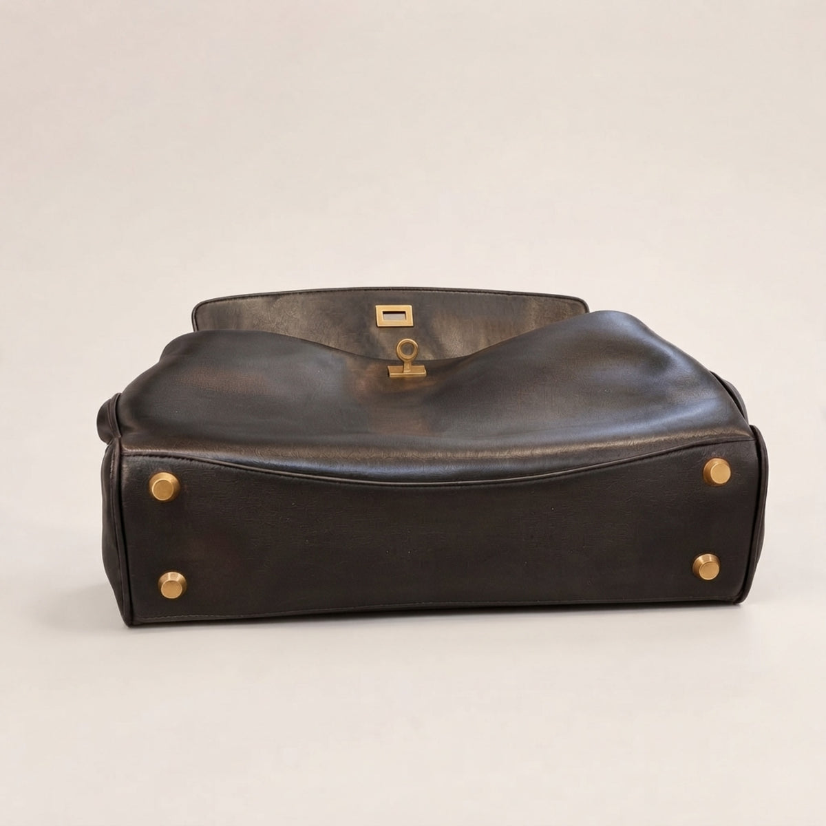 A dark brown leather handbag with gold-tone hardware, shown from a side angle against a neutral light gray background.