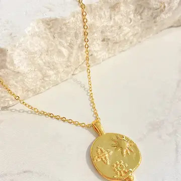 Gold medallion pendant displayed on a textured stone surface, showing the embossed sun and floral design.