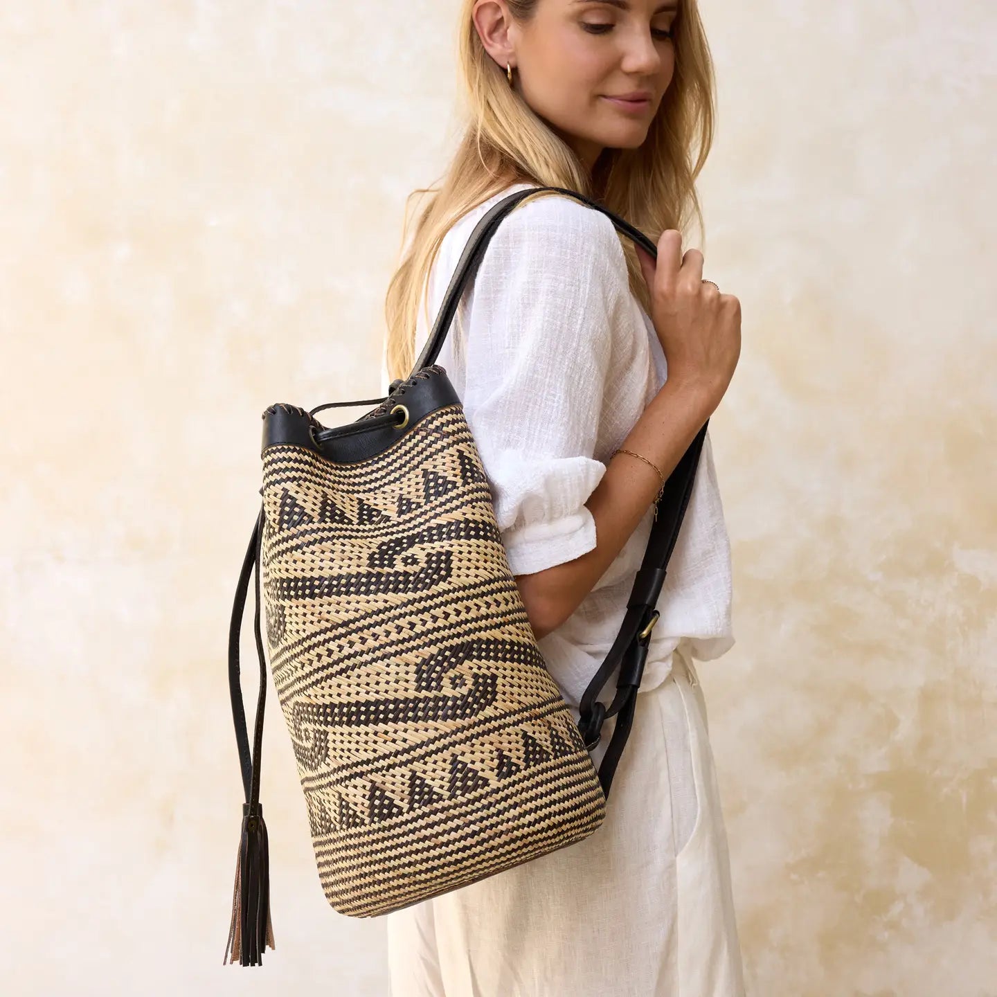 “Woman wearing a handwoven Borneo rattan bucket bag with black leather trim and shoulder strap.”