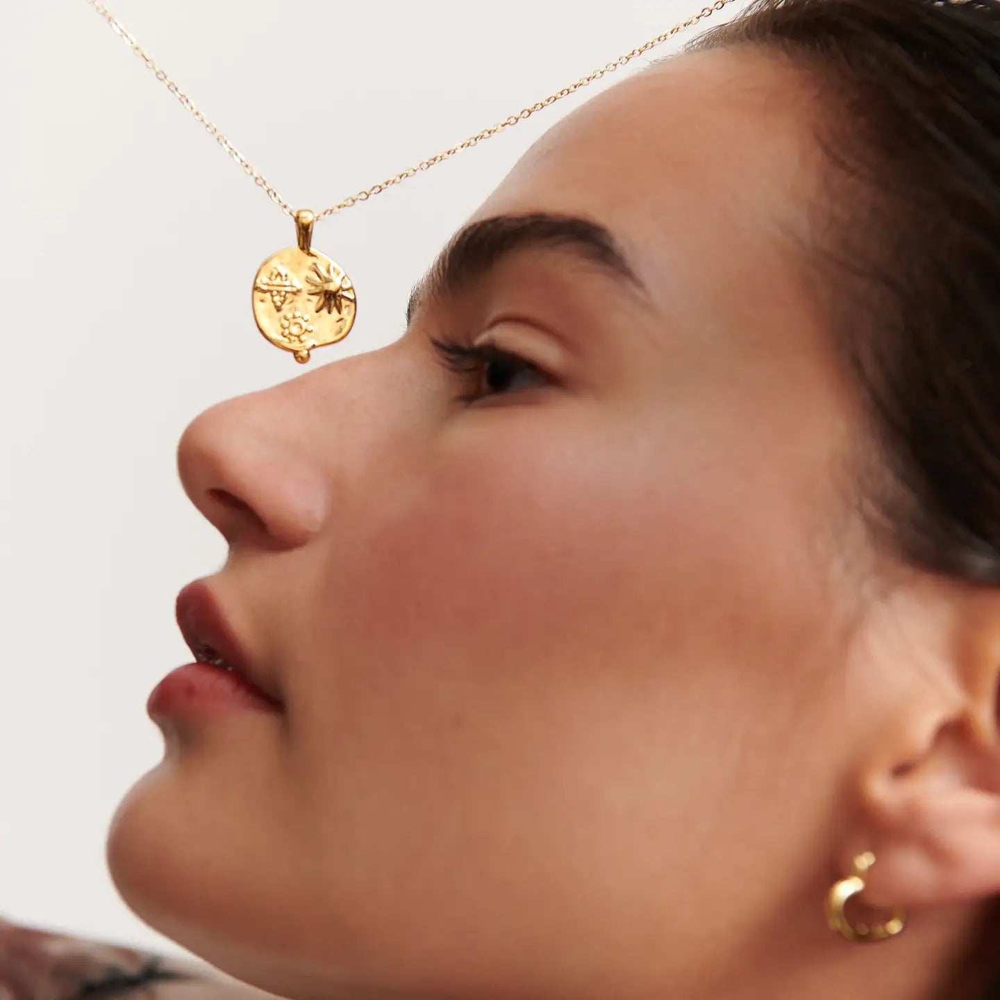 Gold medallion necklace with embossed sun and floral symbols resting near a model’s face, highlighting the pendant detail.