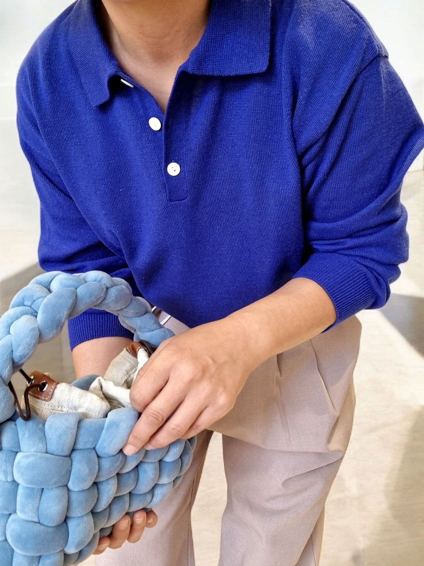 “Close-up of royal blue cotton top with sleeves rolled up, model holding a textured blue bag”