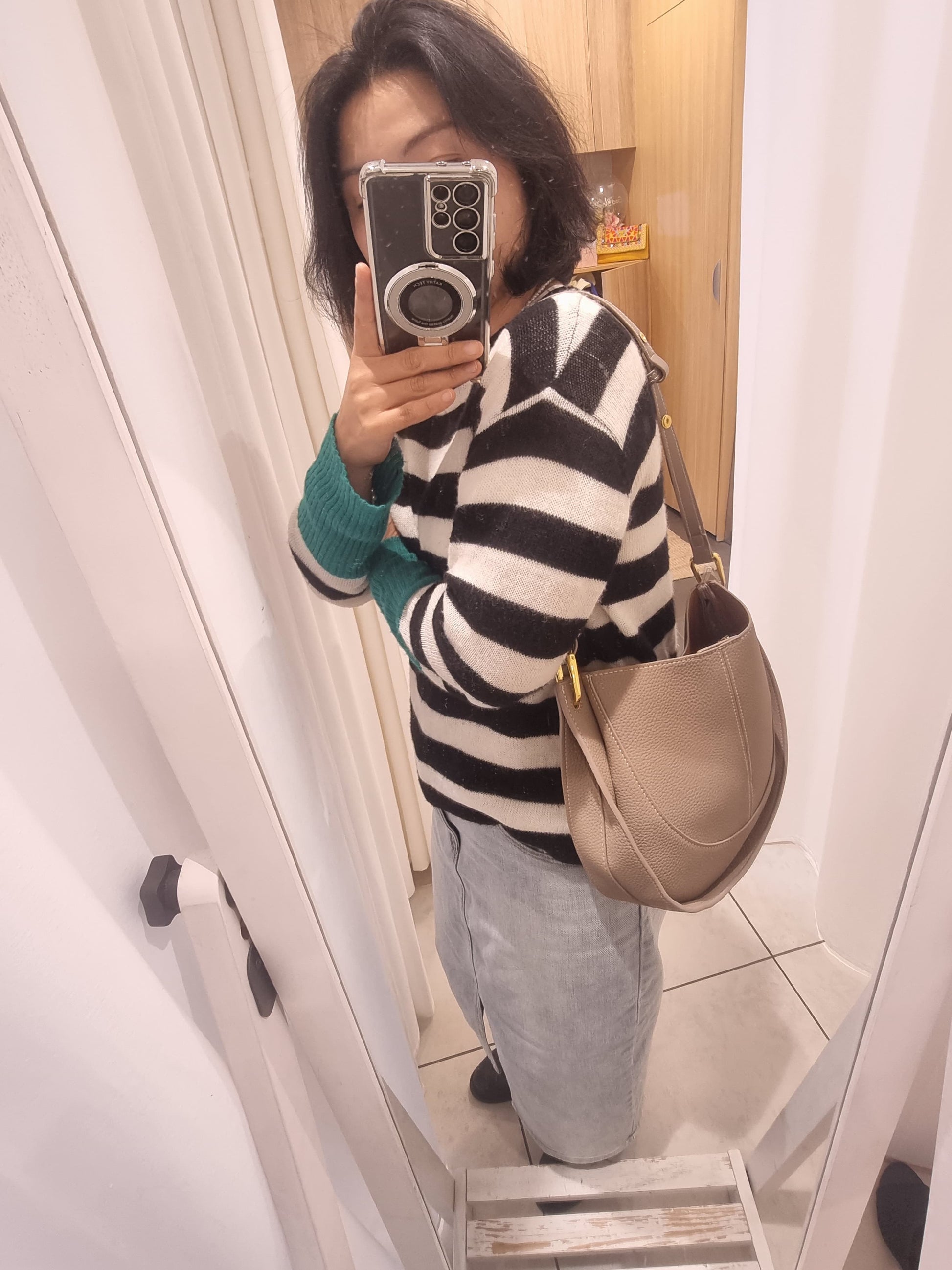 Woman wearing a beige leather shoulder bag with striped knit top