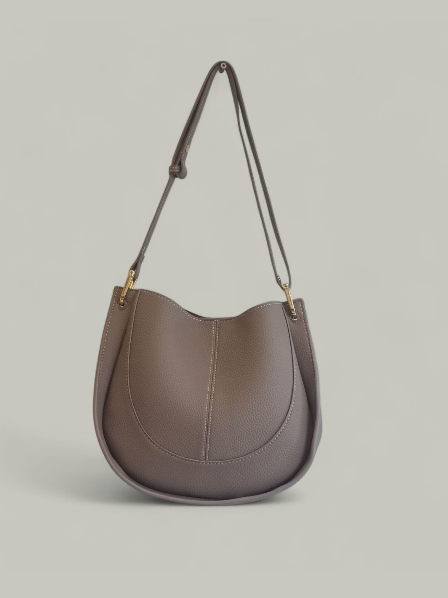 Beige leather shoulder bag hanging on a neutral background
