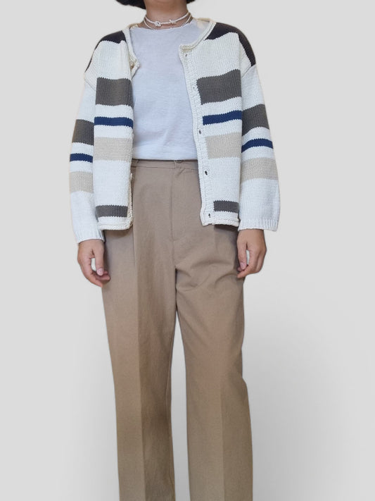 “Woman wearing blue, cream, and charcoal striped cotton cardigan over a white top with beige trousers.”