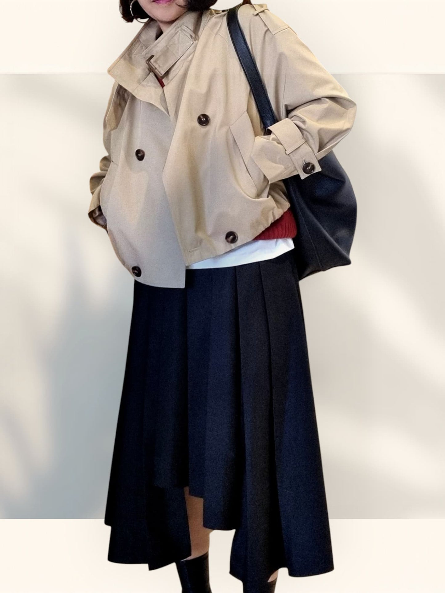 “Beige cropped trench coat with double-breasted buttons styled over layered tops and a navy A-line skirt on a light neutral background.”