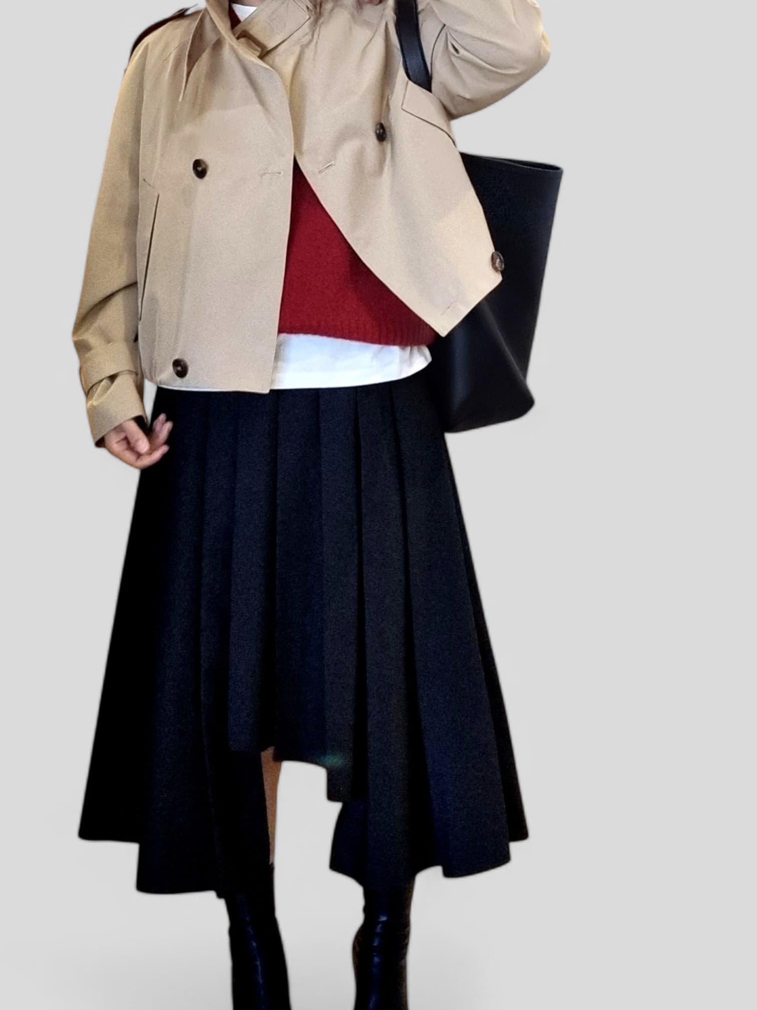 “Beige cropped trench coat styled with a red knit layer, white inner top, and black pleated midi skirt on a neutral background.”