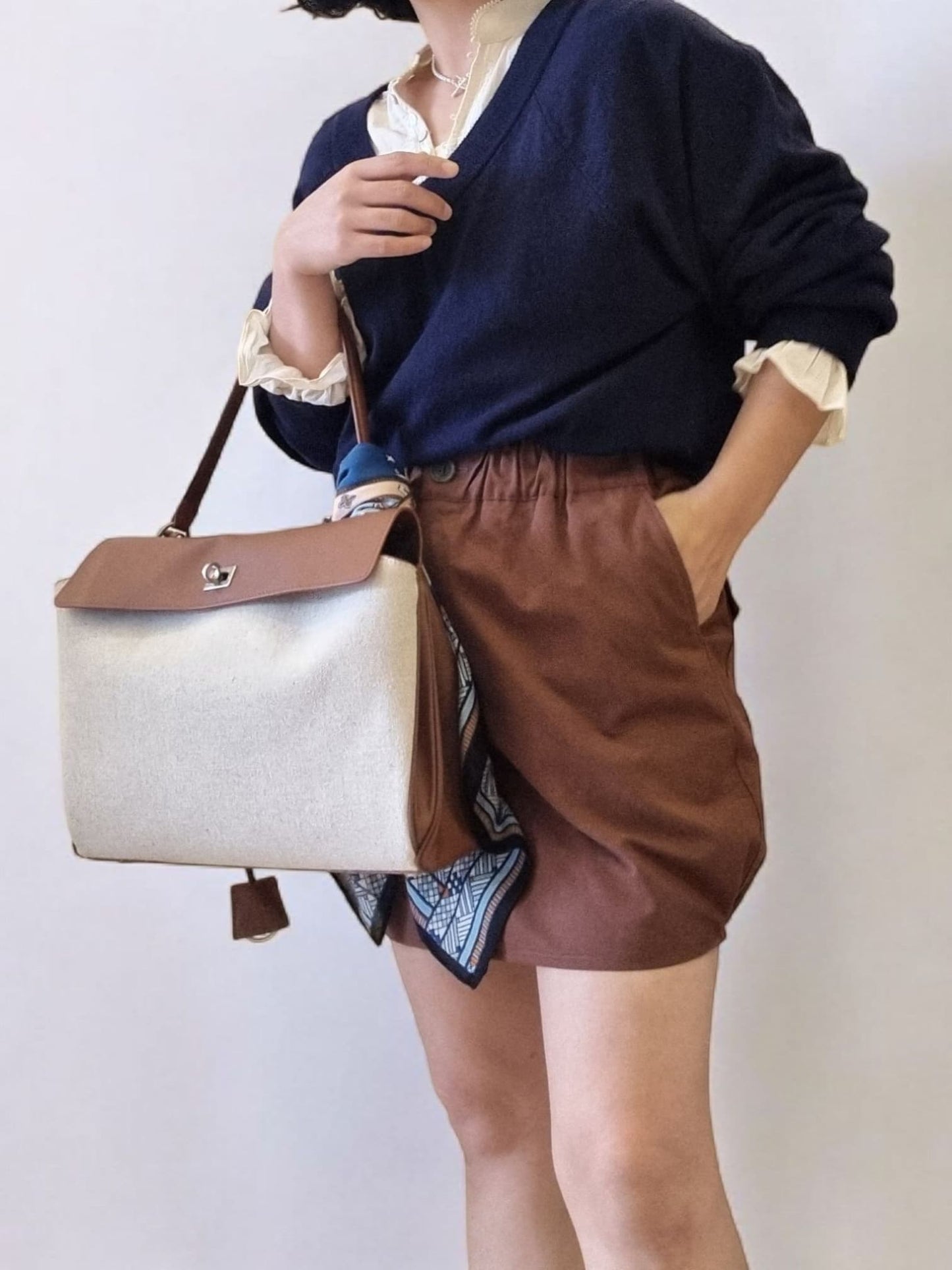 Side view of model in brown pumpkin skirt holding handbag.