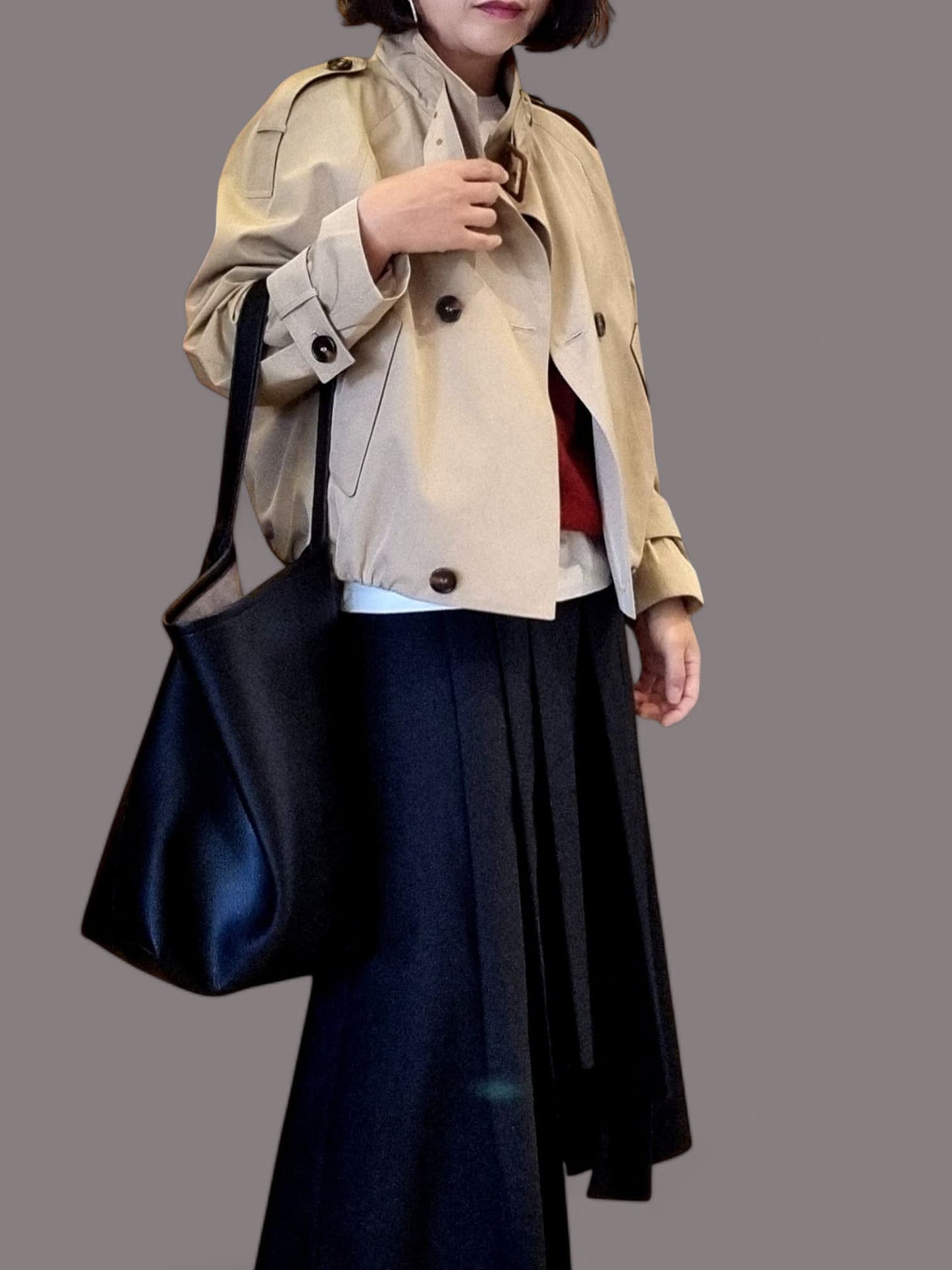 “Beige cropped trench coat styled with a navy pleated skirt and black shoulder bag on a neutral background.”