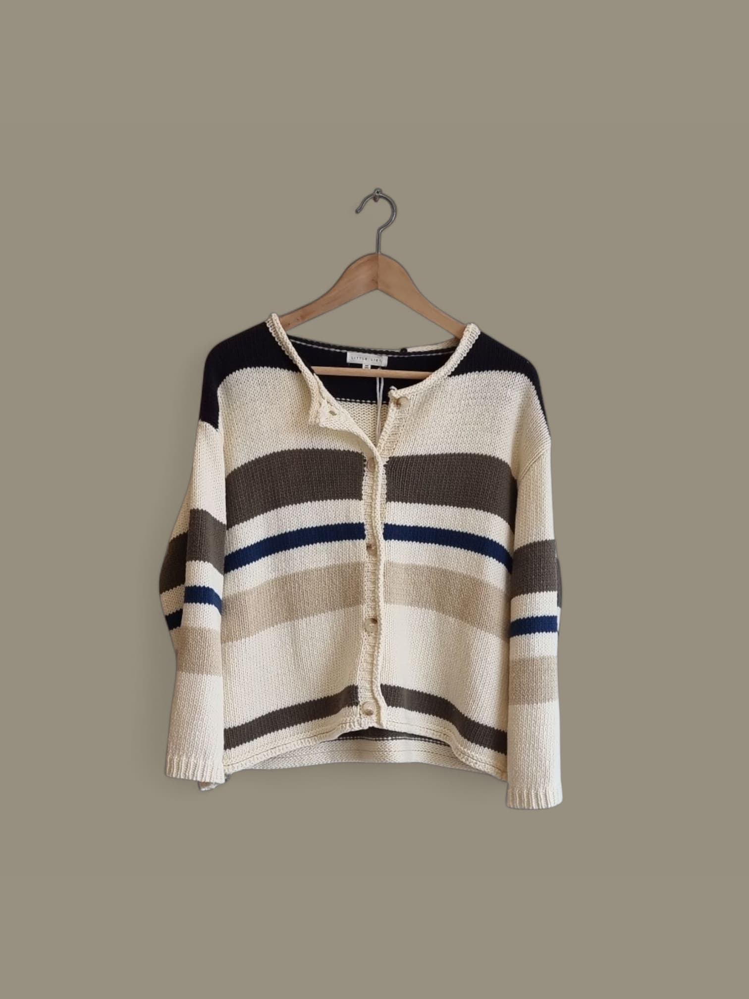 “Striped cotton cardigan in blue, cream, and charcoal hanging on a wooden hanger.”
