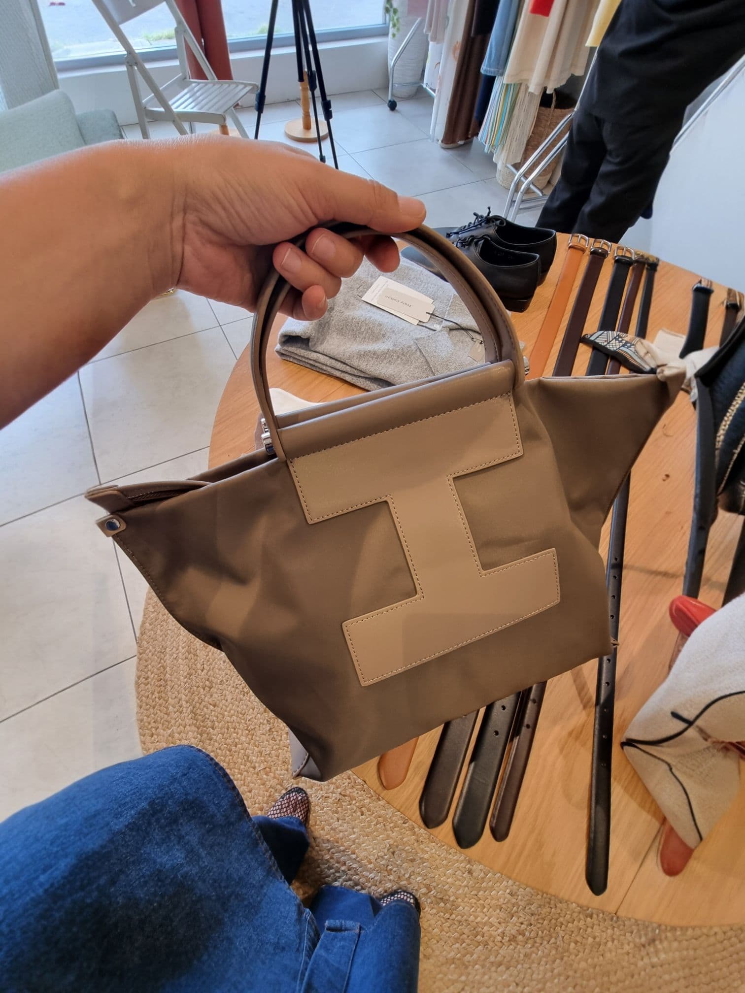 Woman holding brown EB tote bag indoors, showcasing handle and material texture.