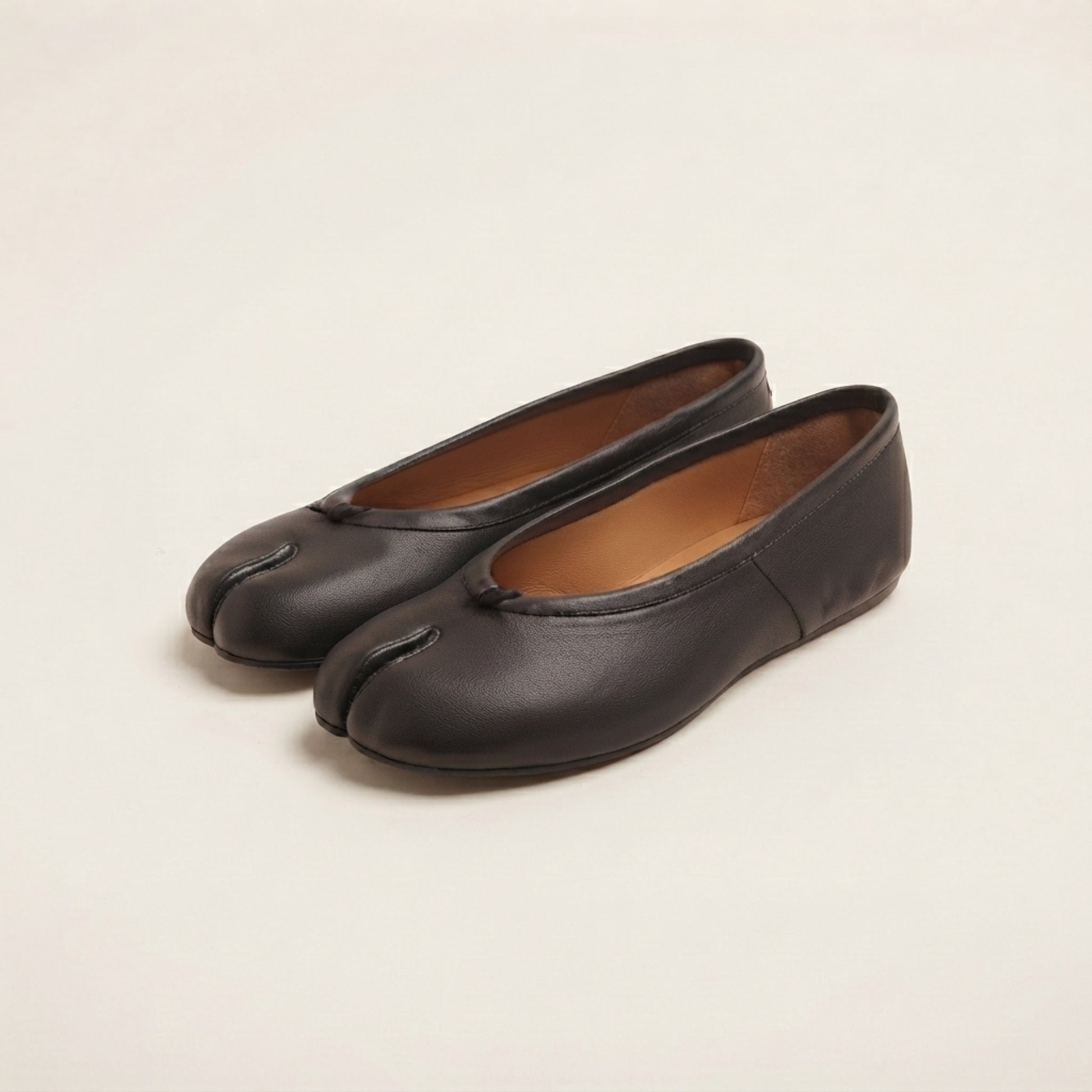 A pair of black leather tabi-style flats with a split toe design, displayed on a clean, light beige background.
