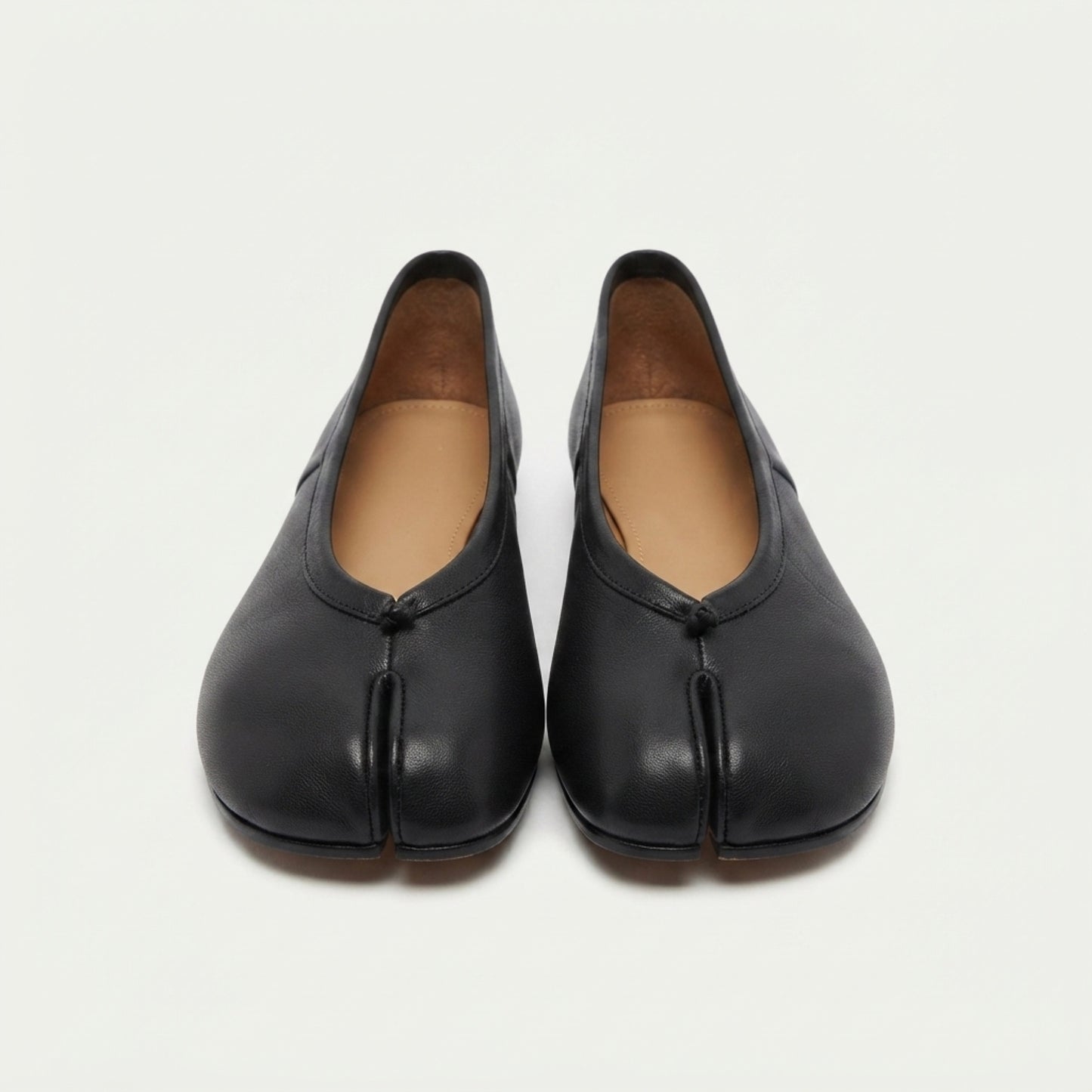A pair of black leather tabi shoes with a traditional split-toe design, shown from the front on a light off-white background.